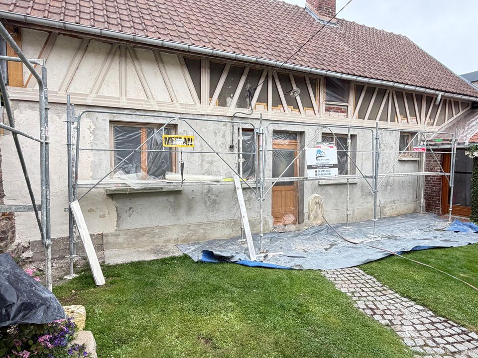 Longère avant travaux : échafaudage monté, enduit piqué et pans de bois mis à nu.