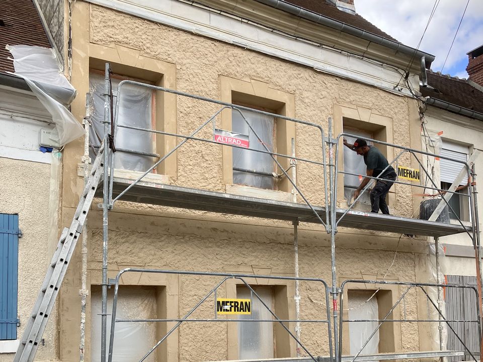 Maison de ville pendant les travaux : échafaudage, protections au sol et enduit en cours d'application.