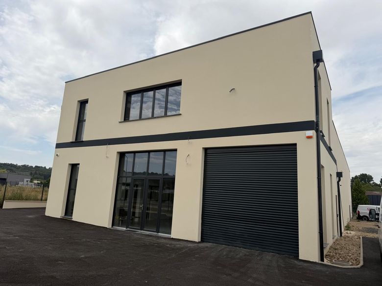 Bâtiment professionnel neuf, façade en enduit monocouche beige et bandeau anthracite.