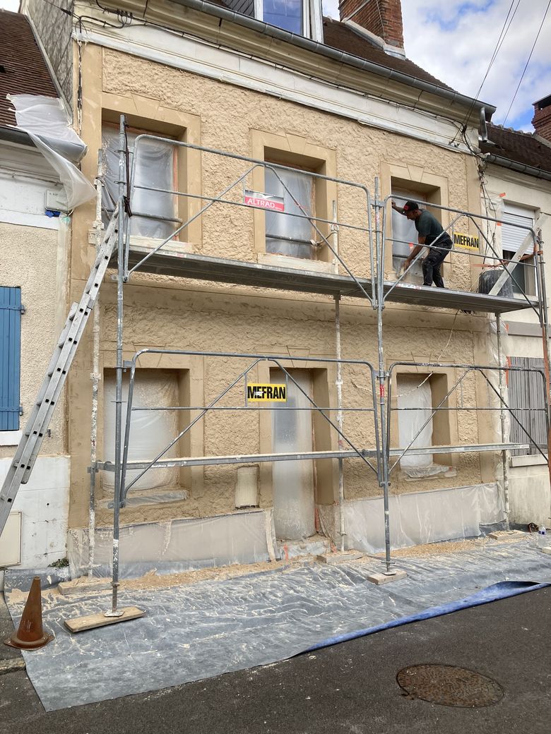 Façade en cours d'enduit, compagnon sur échafaudage, sol et menuiseries protégés.