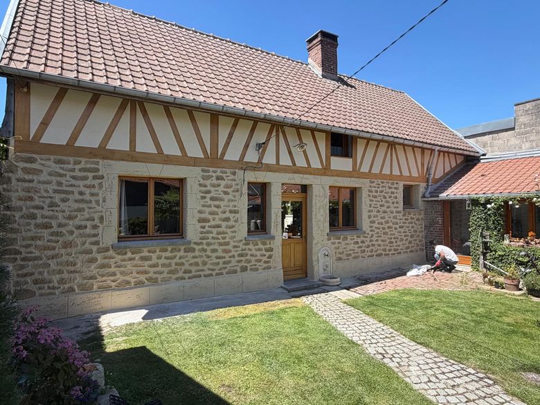 Longère à colombages rénovée, soubassement en pierre et jardin au premier plan.