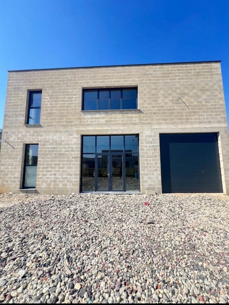 Façade de bâtiment neuf en parement pierre reconstituée avec grandes menuiseries anthracite.